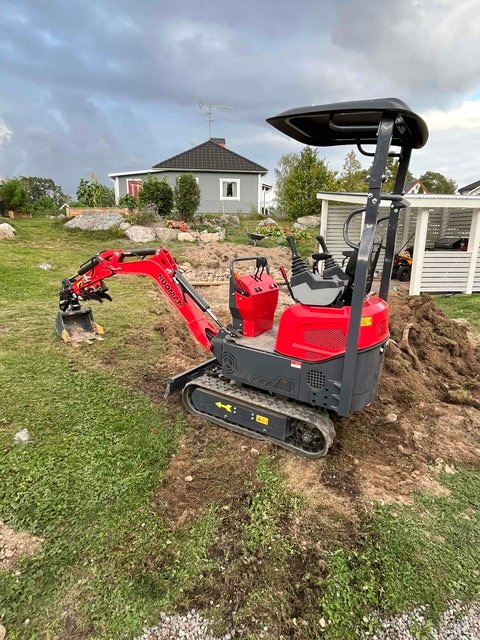 A red canopy mini excavator beside a small excavation on grass.